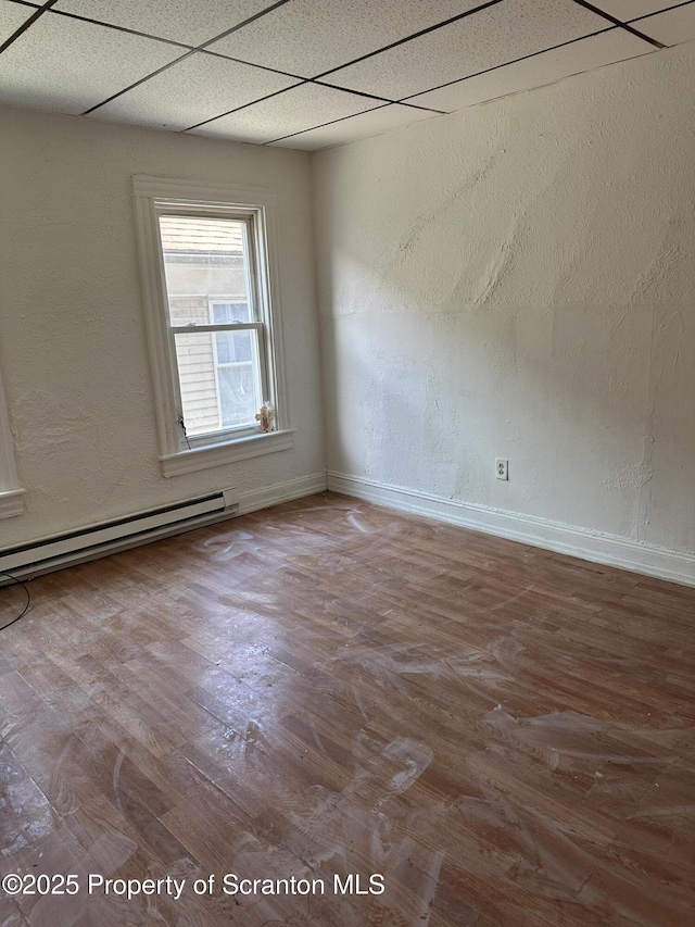 empty room featuring a drop ceiling, wood finished floors, a baseboard radiator, baseboards, and a textured wall