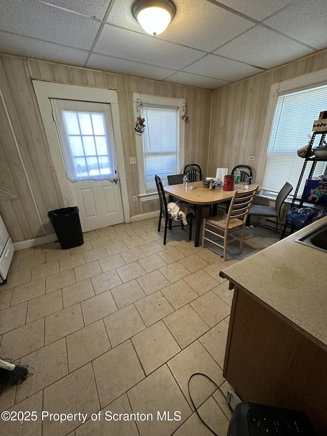 dining area with a drop ceiling and wood walls