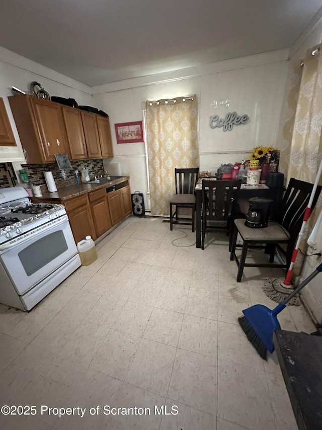 kitchen with tasteful backsplash, brown cabinets, white range with gas stovetop, and a sink