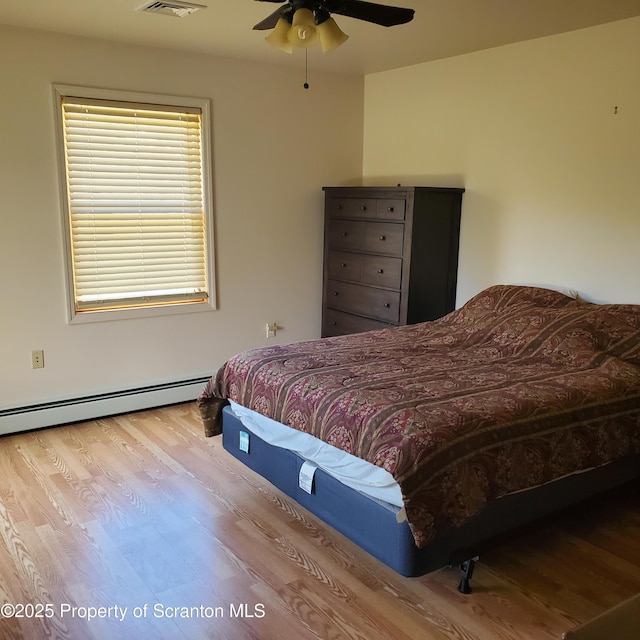 bedroom featuring visible vents, baseboard heating, wood finished floors, and a ceiling fan