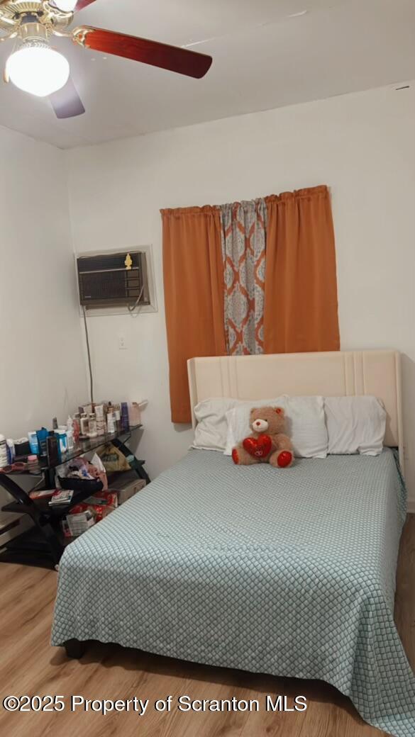 bedroom featuring ceiling fan, wood-type flooring, and a wall mounted air conditioner