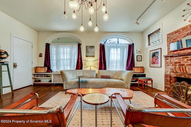 living room with a notable chandelier, dark hardwood / wood-style floors, and a brick fireplace