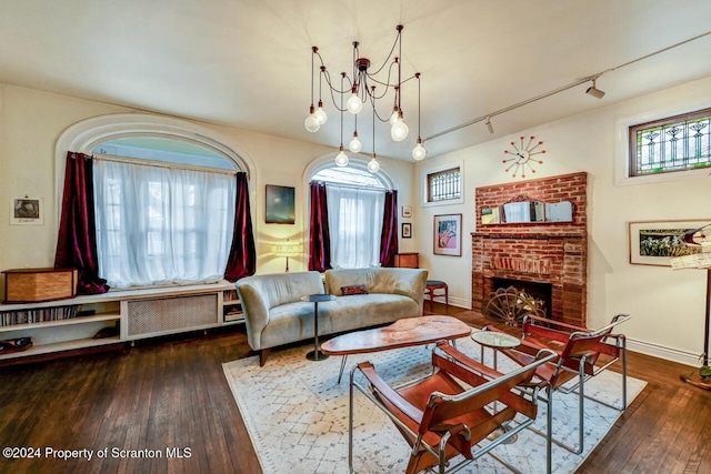 living room featuring dark hardwood / wood-style floors, a chandelier, radiator, and a brick fireplace