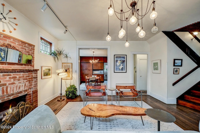 living room with track lighting, a chandelier, dark hardwood / wood-style floors, and a brick fireplace