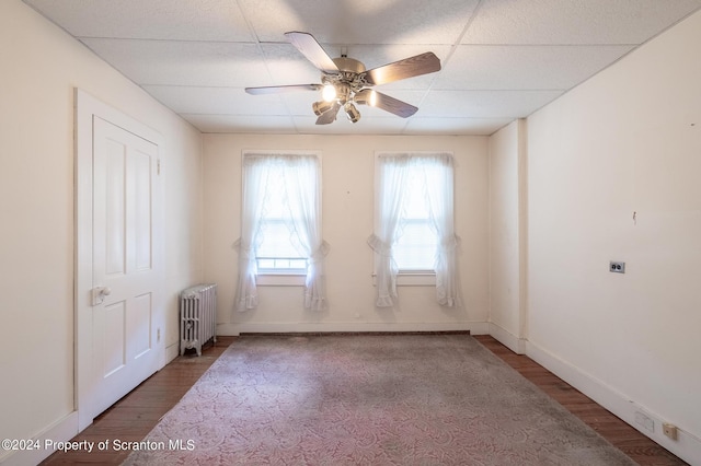 unfurnished room with ceiling fan, a paneled ceiling, radiator heating unit, and hardwood / wood-style flooring