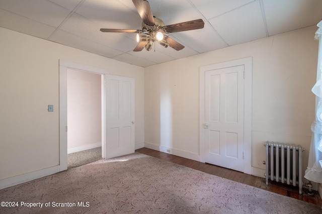 unfurnished bedroom with a paneled ceiling, dark hardwood / wood-style flooring, radiator heating unit, and ceiling fan