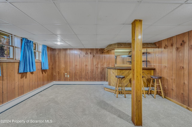 basement with carpet flooring, a drop ceiling, wood walls, and bar