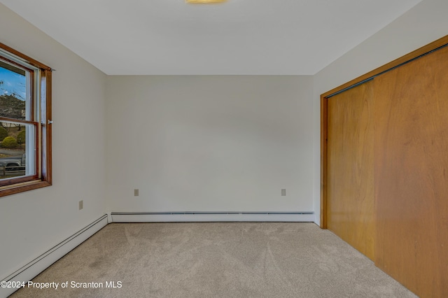 unfurnished bedroom featuring baseboard heating, light carpet, and a closet