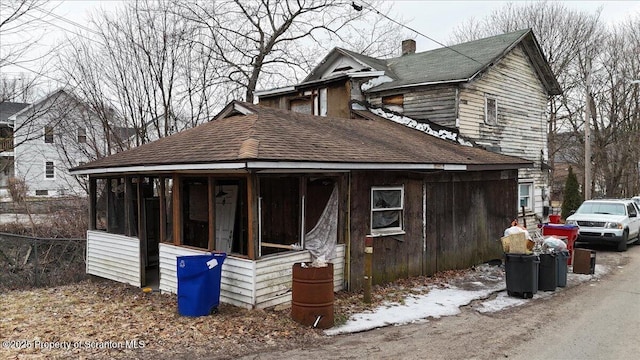 view of front facade featuring a chimney, a sunroom, and roof with shingles