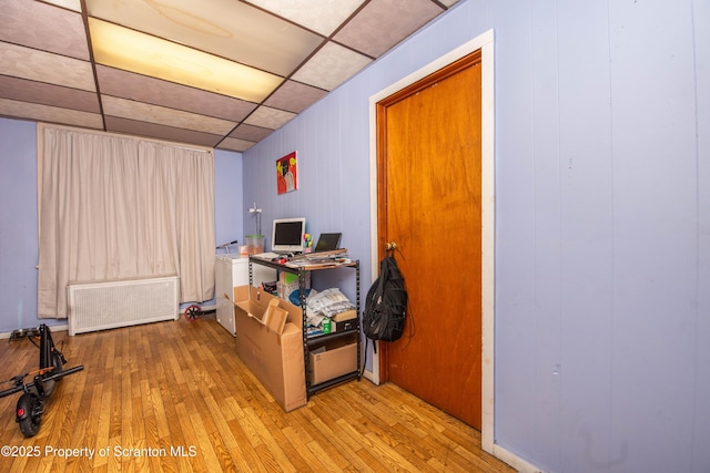 interior space with a drop ceiling, radiator heating unit, and hardwood / wood-style floors