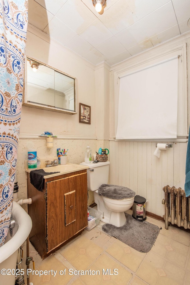 bathroom with a wainscoted wall, toilet, a shower with curtain, radiator heating unit, and vanity