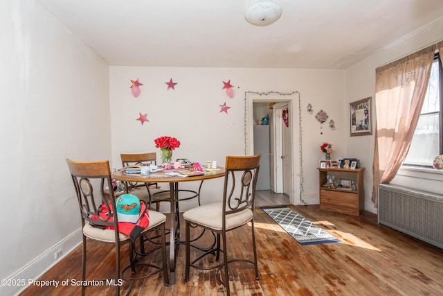 dining area with radiator heating unit, baseboards, and wood finished floors