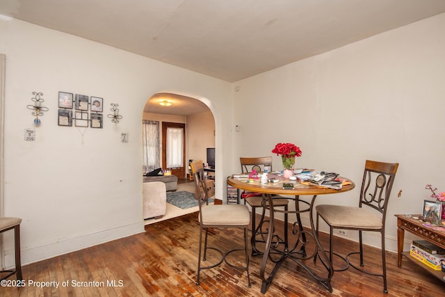 dining space featuring arched walkways, baseboards, and wood-type flooring