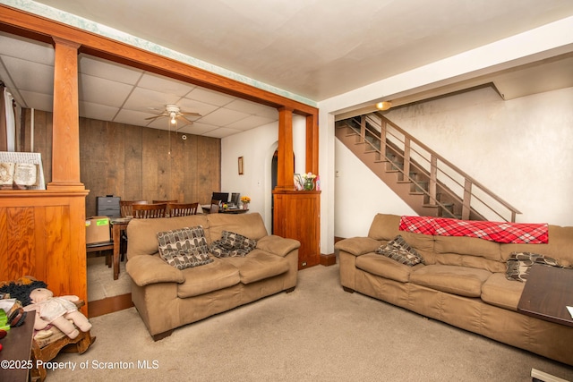 carpeted living room featuring a drop ceiling, ceiling fan, and stairs