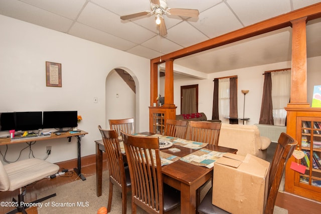 dining room featuring arched walkways, a drop ceiling, baseboards, and a ceiling fan