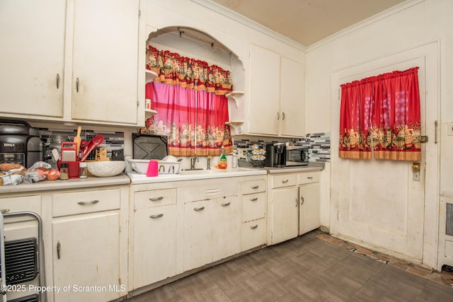 kitchen featuring tasteful backsplash, stainless steel microwave, light countertops, ornamental molding, and a sink