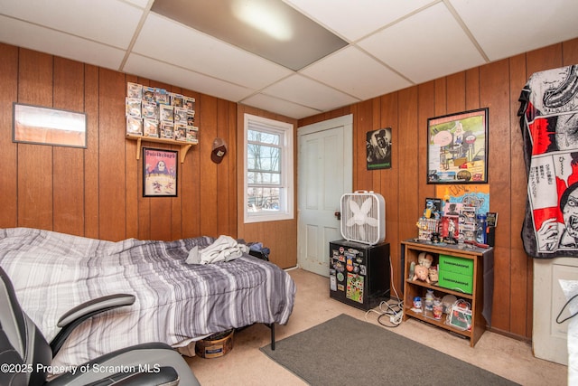 bedroom featuring a drop ceiling, carpet floors, and wood walls