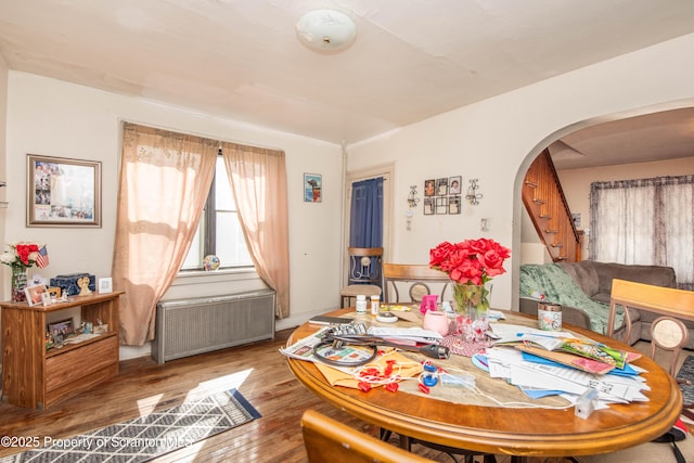 dining area featuring arched walkways, stairway, radiator heating unit, and wood finished floors