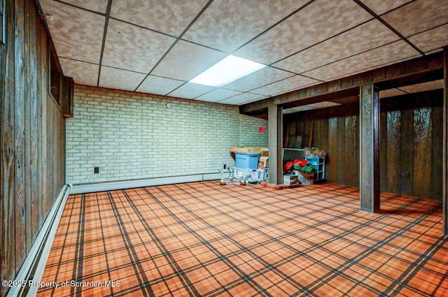 basement with a paneled ceiling, brick wall, and baseboard heating