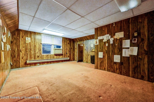 basement with baseboard heating, cooling unit, carpet floors, a drop ceiling, and wood walls