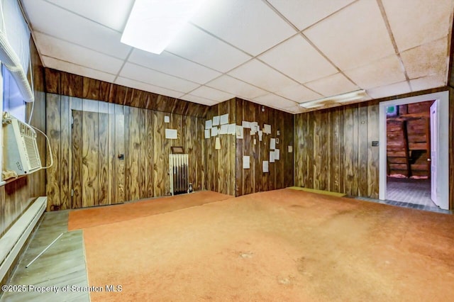 spare room with wooden walls, a paneled ceiling, baseboard heating, and carpet flooring