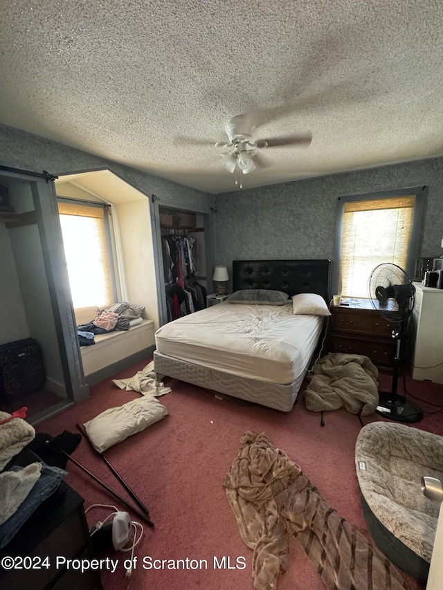 carpeted bedroom featuring a textured ceiling, ceiling fan, multiple windows, and a closet