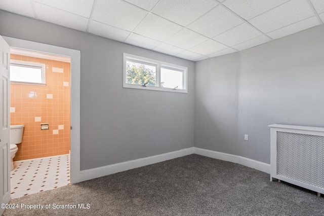 spare room with radiator heating unit, dark carpet, and a drop ceiling