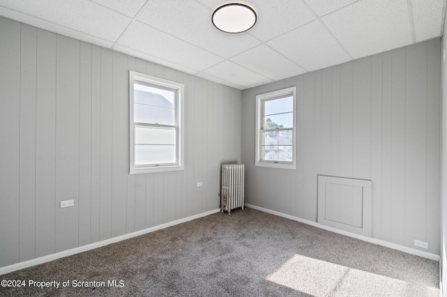 carpeted spare room with a paneled ceiling, radiator heating unit, and wooden walls