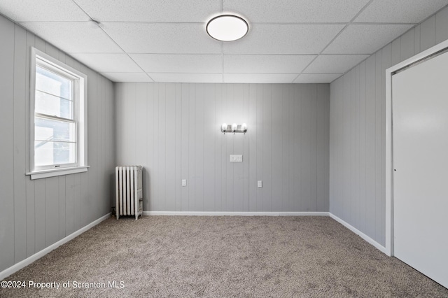 spare room featuring a paneled ceiling, carpet flooring, wood walls, and radiator