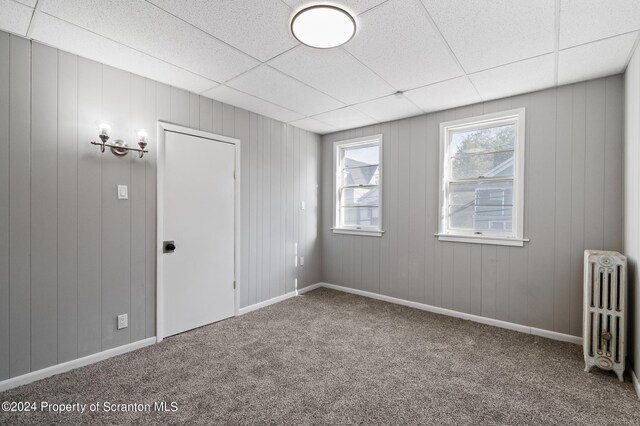 unfurnished room with radiator heating unit, carpet floors, a drop ceiling, and wooden walls