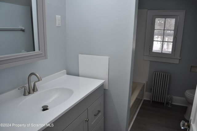 bathroom featuring hardwood / wood-style floors, vanity, toilet, a tub to relax in, and radiator heating unit