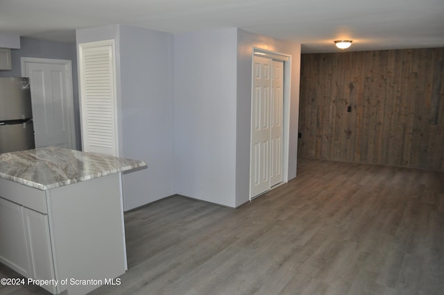 kitchen with wooden walls, hardwood / wood-style floors, white cabinets, and light stone countertops