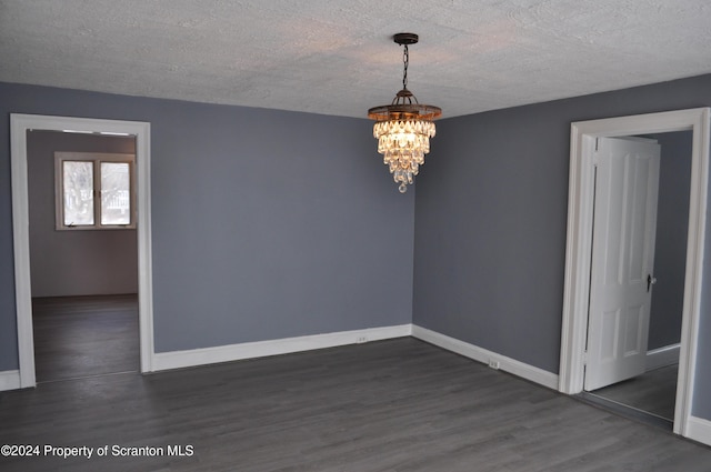 empty room with dark hardwood / wood-style floors, a textured ceiling, and a chandelier