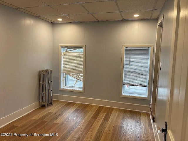 empty room featuring hardwood / wood-style floors, a drop ceiling, and radiator