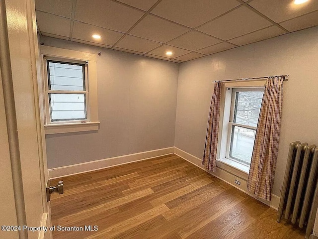 empty room with radiator heating unit, a drop ceiling, and wood-type flooring