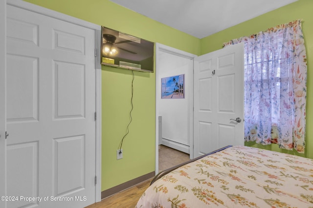 bedroom with light hardwood / wood-style floors, a closet, and a baseboard heating unit