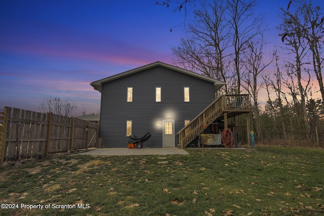 back house at dusk with a patio, a wooden deck, and a lawn