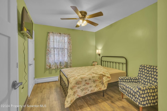 bedroom with ceiling fan, wood-type flooring, and a baseboard heating unit