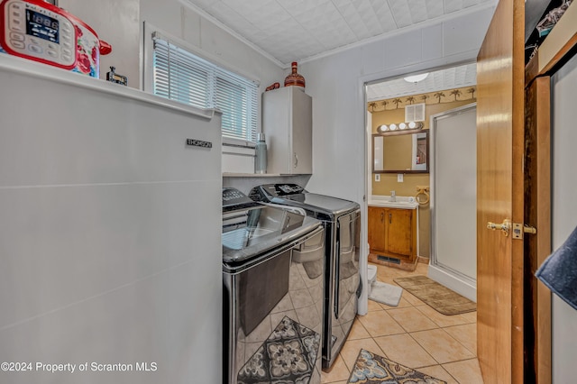 clothes washing area with cabinets, sink, crown molding, light tile patterned floors, and washing machine and clothes dryer