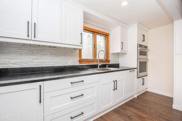 kitchen with dark countertops, white cabinetry, a sink, and stainless steel double oven