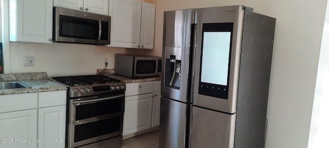 kitchen with stainless steel appliances, light tile patterned flooring, and white cabinets