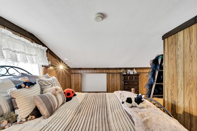 bedroom with a textured ceiling, vaulted ceiling, and wood walls