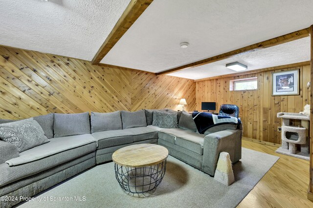 living room featuring beam ceiling, a textured ceiling, wooden walls, and light hardwood / wood-style flooring