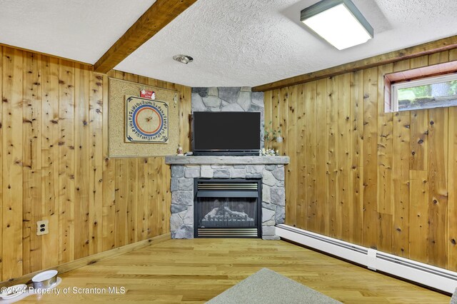 unfurnished living room with beam ceiling, a baseboard heating unit, wood walls, wood-type flooring, and a fireplace