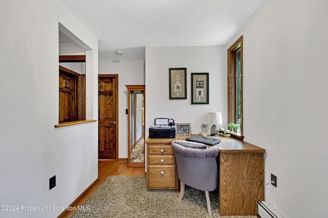 office area with a baseboard radiator, a textured ceiling, and light hardwood / wood-style floors