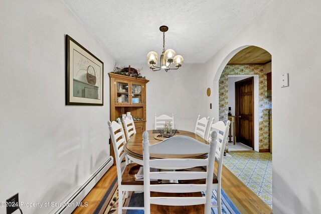 dining area with wood-type flooring, a textured ceiling, a baseboard radiator, and a notable chandelier