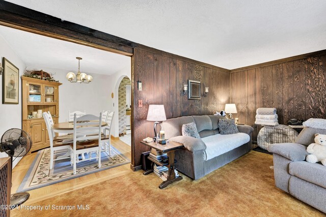 carpeted living room featuring a textured ceiling, wood walls, beam ceiling, and a chandelier