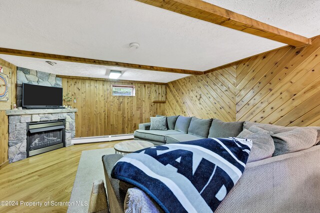 living room with a textured ceiling, a baseboard heating unit, hardwood / wood-style flooring, beamed ceiling, and a stone fireplace