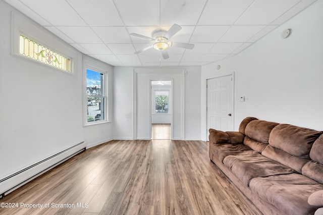 unfurnished living room with a paneled ceiling, hardwood / wood-style flooring, baseboard heating, and ceiling fan