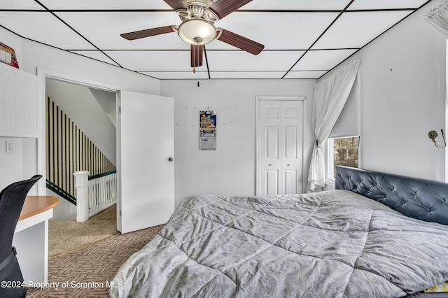 carpeted bedroom with a paneled ceiling, a closet, and ceiling fan